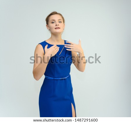 Photo studio portrait of a pretty young woman girl in a beautiful blue dress on a white background. He stands right in front of the camera, explains with emotion.