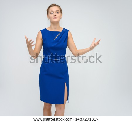 Full length studio portrait photo of a cute young woman girl in a beautiful blue dress on a white background. He stands right in front of the camera, explains with emotion.