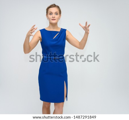 Full length studio portrait photo of a cute young woman girl in a beautiful blue dress on a white background. He stands right in front of the camera, explains with emotion.