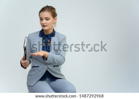 Studio photo a waist-high portrait of a cute young woman girl in a business suit on a white background with a folder in hands. Sits in a chair right in front of the camera, explains, with emotions.