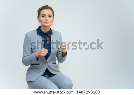Studio photo a waist-high portrait of a pretty young woman girl in a business suit on a white background. Sits in a chair right in front of the camera, explains, with emotions.