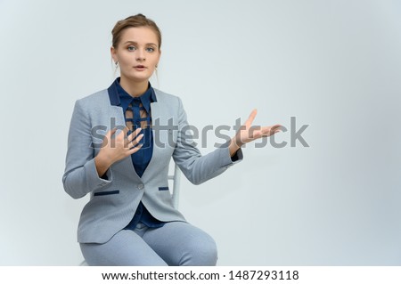 Studio photo a waist-high portrait of a pretty young woman girl in a business suit on a white background. Sits in a chair right in front of the camera, explains, with emotions.