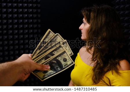 Refusal to receive dollars in the recording Studio. Payment for recording a song at the concert of the singer. The woman turns away from the money on a black background.