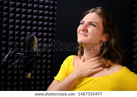 A young woman holding her throat near the microphone, black background. The voice of the singer when recording a song in the music Studio. Voice failure, hoarseness, pain in the vocal cords. Royalty-Free Stock Photo #1487310497