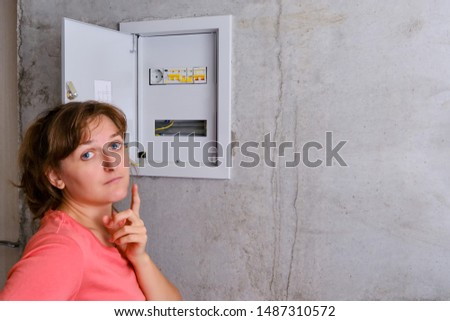 A young woman deep in thought next to the fuse box, copy space. Power outage in the apartment. Distribution board in the house and switch off the switch.