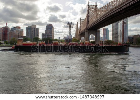 A tug pushes a ship under the Ed Koch Queensboro Bridge.