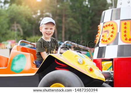 Cute 5 year old boy in a blue baseball cap rides a toy car.