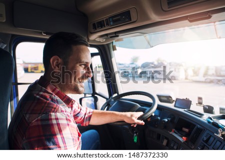 Professional middle aged truck driver in casual clothes driving truck vehicle going for a long transportation route. Royalty-Free Stock Photo #1487372330