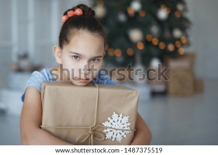 Teenager girl sits near a Christmas tree with a gift box in her hands. New Year. A pleasant surprise.