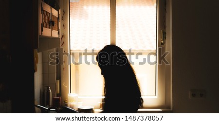 A portrait of a silhouette of an unknown woman with long hair standing in front of a window with rim light from behind the profile Royalty-Free Stock Photo #1487378057