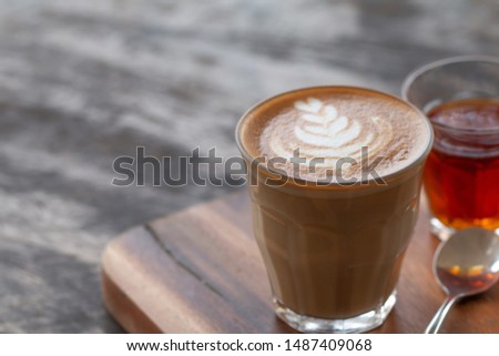 A glass cup of Latte art coffee on wooden desk.