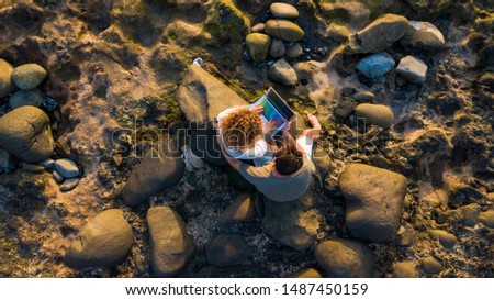 beautiful couple of adults isolated on the beach with their laptop or computer - top view and above - relationship or frienship together