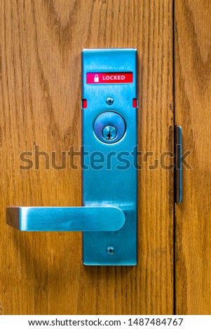 Vertical portrait photo of a door lock and handle in the locked position with the word locked displayed. Picture also displays the door seam and latch bracket.