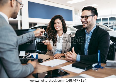 Middle age couple choosing and buying car at car showroom. Car salesman gives them car keys. Royalty-Free Stock Photo #1487497124