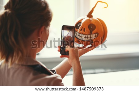 a woman artist prepares for halloween and photographed on smartphone his work painted pumpkin
