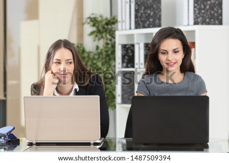 Front view of an envious employee looking her colleague working beside Royalty-Free Stock Photo #1487509394