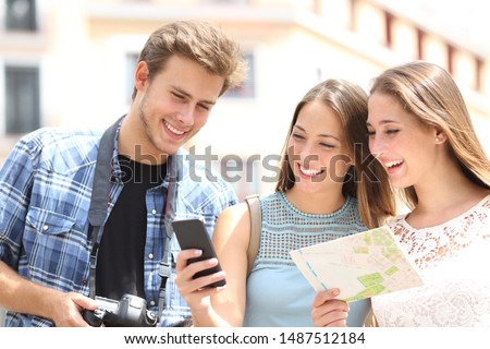 Three happy tourists traveling checking smart phone gps and map in the street on summer vacation