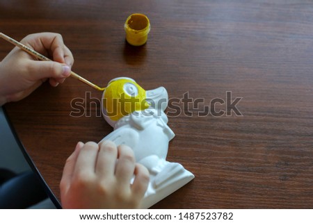 Сhildren's hands paints a duck-shaped alabaster figure in yellow. Hobbies, drawing, creativity. Handmade toy. Decor master class