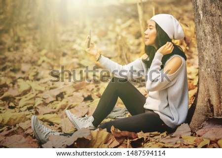 Young woman taking selfie photo with a mobile phone at the autumn park. Autumn Concept. Shot outdoors