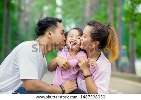 Young parents kissing their daughter while playing together in the park