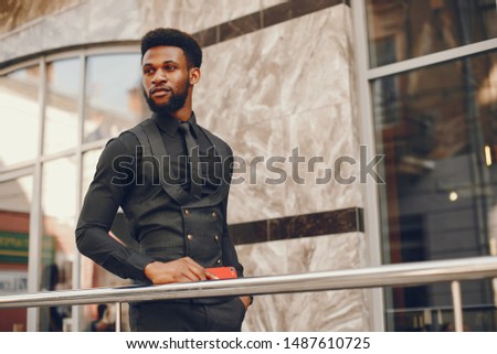 A young and handsome dark-skinned boy in a black suit standing in a city