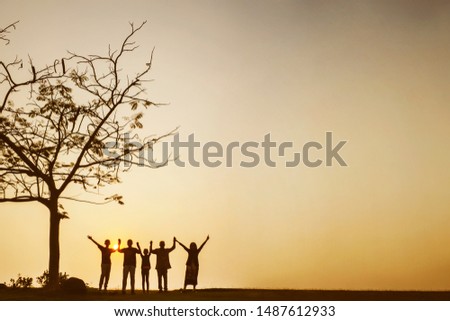 Silhouette of multi generation family looks happy while holding hands together and standing near a tree at sunset time