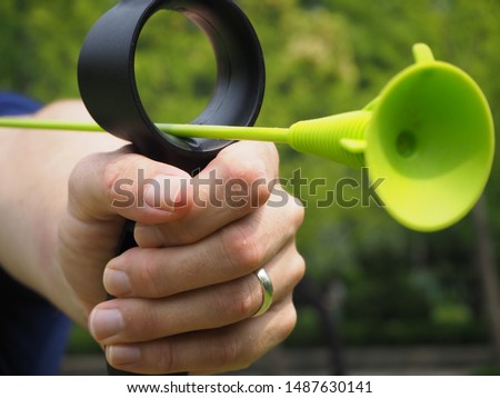 Shanghai/ China - June 16 2019: front-side view close up of a man's hand preparing to shoot a bright green training arrow with the background in soft focus