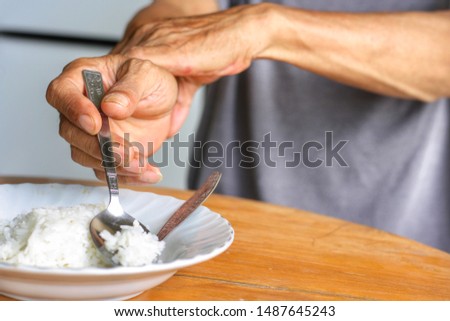 Elderly man is holding his hand while eating because Parkinson's disease.Tremor is most symptom and make a trouble for doing activities such as eat.Health care or elderly concept.Have copy space. Royalty-Free Stock Photo #1487645243