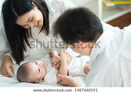 Asian father and mother are playing with new newborn baby on sofa. They are smiling and warm touching to the baby with love. Parents holding both of baby hand. Happy family concept. Royalty-Free Stock Photo #1487660591