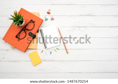 Work space school desktop concept on white wooden table desk with blank notepad and stack of book , glass, pencil, green plant and paper clip, flat lay, Top view with copy space