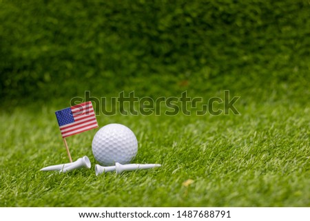 Golf ball with flag of America and tee are on green grass.