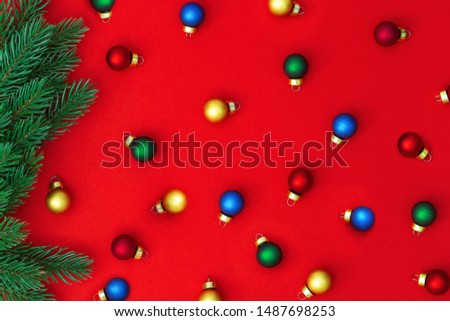 Small multi-colored Christmas balls falling from pine branch on red paper. Christmas background. Top view. 