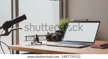 Cozy photographer home-office with open blank screen laptop, vintage camera and office decorations on wooden table 