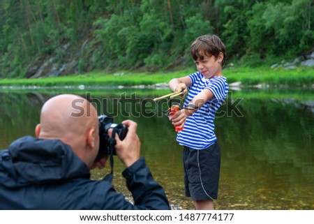 9 year old boy model posing for a photographer outdoors. 
holding a slingshot