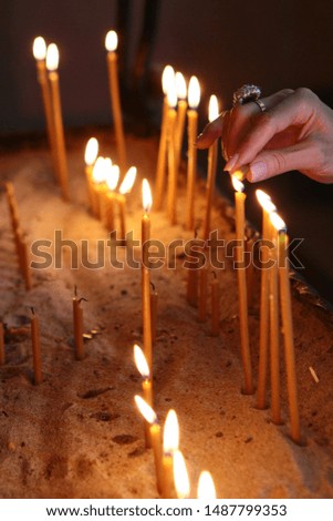 A female hand with a ring lights a candle in a church. The concept of faith in God. Photo without a face.