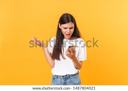 Image of uptight brunette woman wearing basic clothes expressing discontent while holding cellphone isolated over yellow background Royalty-Free Stock Photo #1487804021