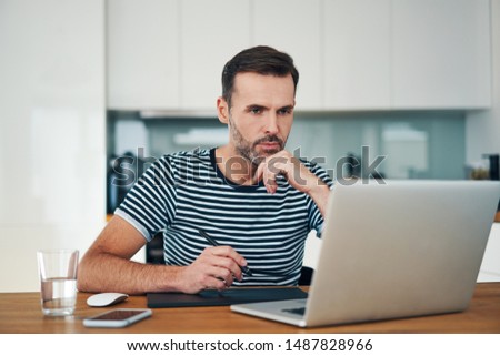 Thoughtful graphic designer working from home with graphics tablet and laptop