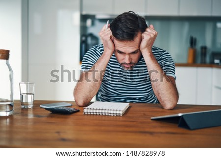 Sad man looking at notebook with home budget and stressing over money Royalty-Free Stock Photo #1487828978