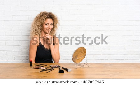 Young woman with lots of makeup brush in a table doing silence gesture