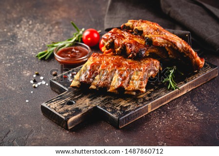 Grilled pork ribs on a wooden cutting board on a brown background Royalty-Free Stock Photo #1487860712