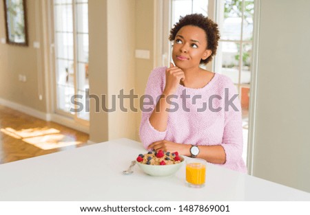 Young african american woman having healthy breakfast in the morning at home with hand on chin thinking about question, pensive expression. Smiling with thoughtful face. Doubt concept.