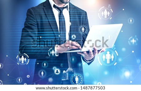 Unrecognizable man in suit using laptop with double exposure of HUD social network interface. Concept of HR and social media. Toned image