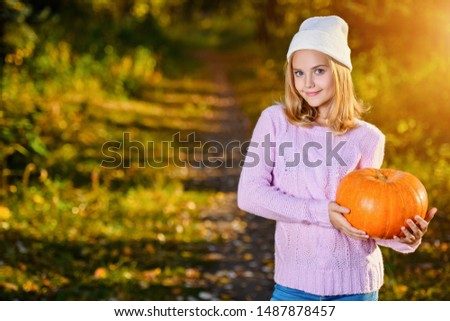 A pretty young girl outdoor with a pumpkin. Autumn fashion, beauty.