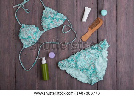 Sea holidays / travel concept - blue beautiful swimsuit and accessories: wooden hairbrush, sunscreen, bottles with cream on wooden background