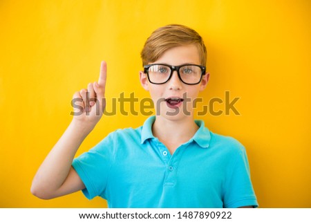 Portrait of stylish little boy with finger pointed up. Kid on yellow blackboard. Success, bright idea, creative ideas and innovation technology concept