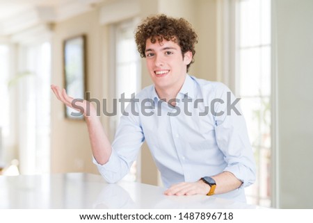 Young business man with curly read head smiling cheerful presenting and pointing with palm of hand looking at the camera.