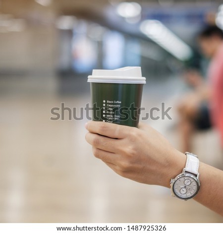 Woman hand holding green coffee paper cup, drinking hot coffee in the city indoor. business and lifestyle concept