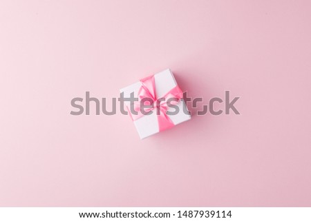 Present or gift box with pink satin bow on pink paper background, top view. Valentines day greeting card, black friday sale, congratulations concept. Flat lay style