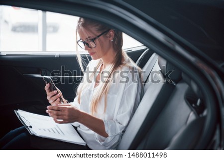 Taking a picture. Smart businesswoman sits at backseat of the luxury car with black interior.