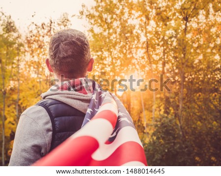 Attractive guy holding a US flag against the background of yellow trees and the setting sun. National holiday concept